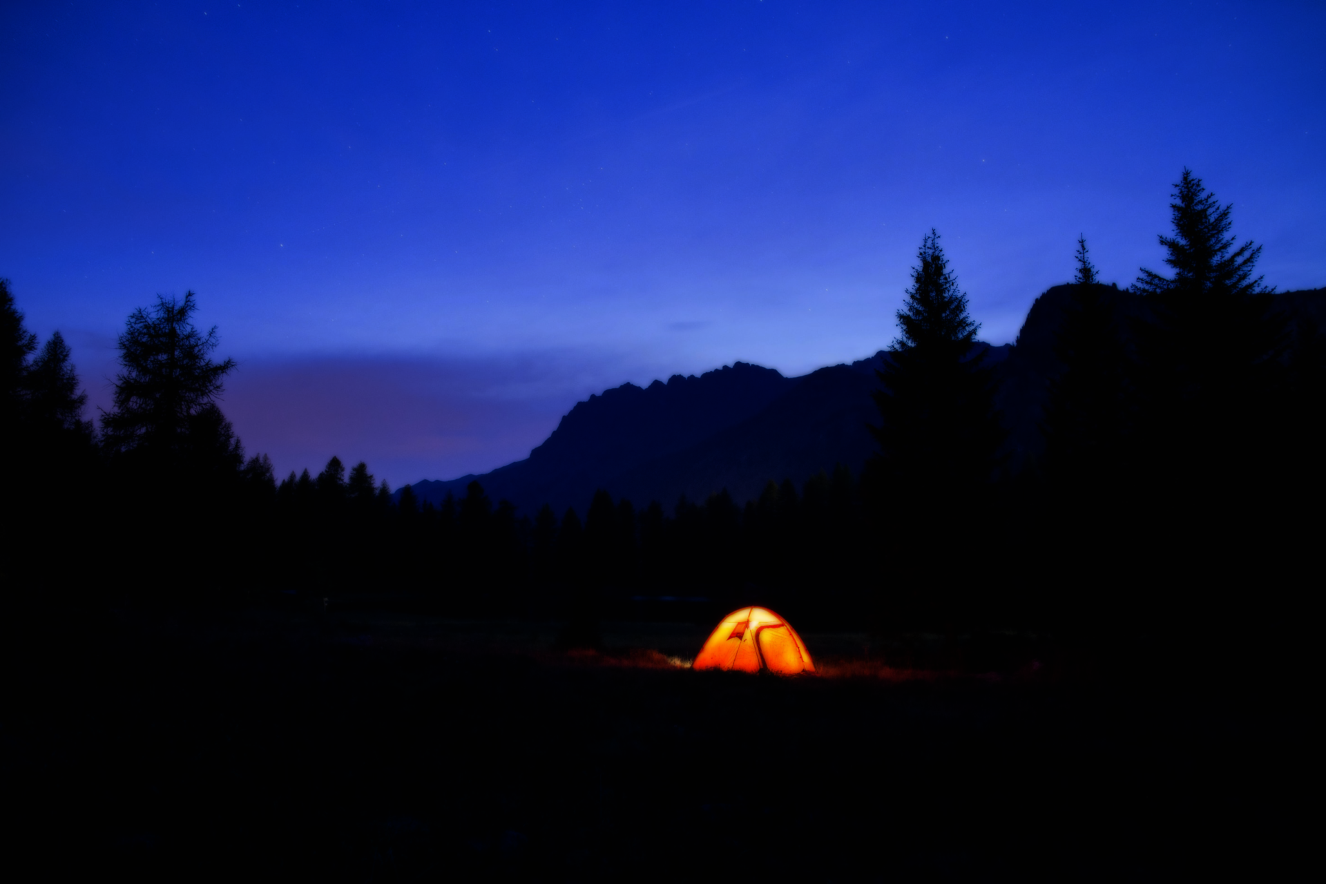Image of a light within a tent at a camping spot in the mountains at dusk.