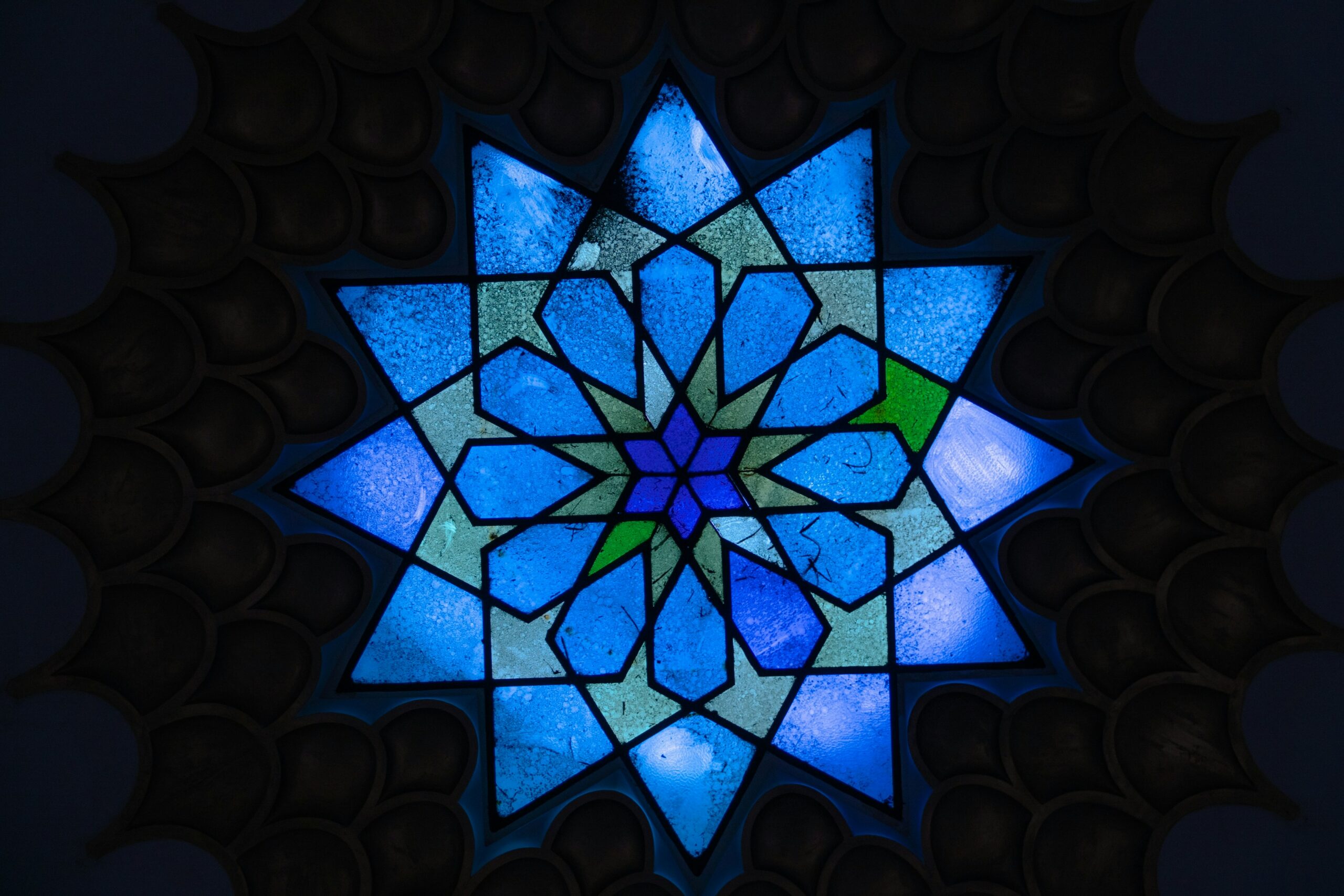 A photo of a blue, multi-pointed star, stained glass window in a Jewish temple.