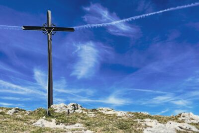 A photo of cross made of iron railings, set on a hill against a cloudy blue sky.