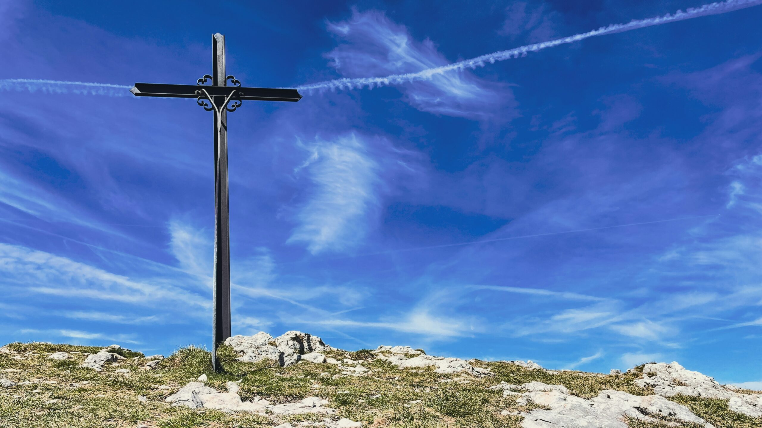 A photo of cross made of iron railings, set on a hill against a cloudy blue sky.