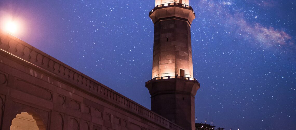 A photo of a prayer mosque with a tower against a night blue sky with stars.
