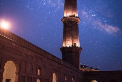 A photo of a prayer mosque with a tower against a night blue sky with stars.